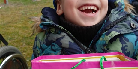 Powiększ grafikę: Uśmiechnięty chłpiec w kolularach trzyma torbę z prezentem.