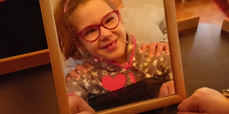 Powiększ grafikę: Usmiechnięta dziewczynka w okularach odbijająca się w lustrze