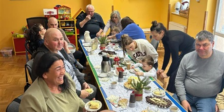 Powiększ grafikę: Dziadkowie i Babcie siedzą przy stole, jedzą ciasto i piją kawę.