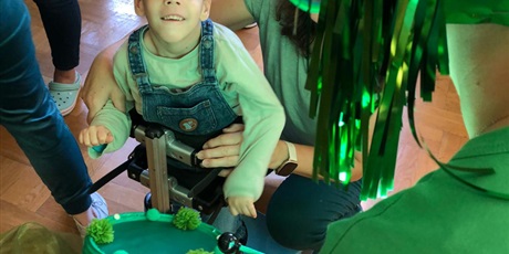 Powiększ grafikę: chłopczyk w zielonym ubraniu patrzy na dorosłego w zielonej peruce