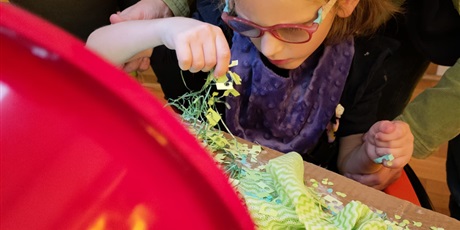 Powiększ grafikę: Dziewczynka w okularach przykleja zieloną bibułę do kartonu