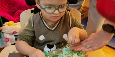 Powiększ grafikę: Chłopiec w okularach przykleja zieloną bibułę do kartonu