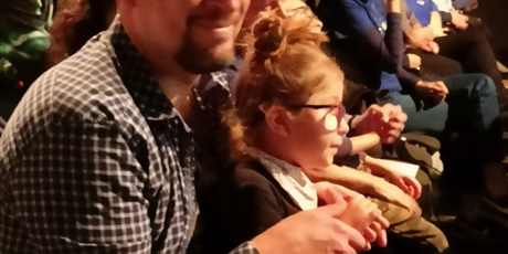 Powiększ grafikę: dziewczynka w okularach zapatrzona na scenę, z tyłu asystuje jej tato