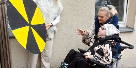 Powiększ grafikę: Dziecko siedzi przed dużym zółto-czarnym kołem. asystenka pomaga wykonać ruch ręką