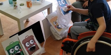 Powiększ grafikę: Dziecko na wózku wrzuca śmieci do pojemników, uczy się sortować