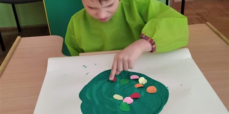 Powiększ grafikę: chłopiec maluje palcami, zieloną farbą piłkę